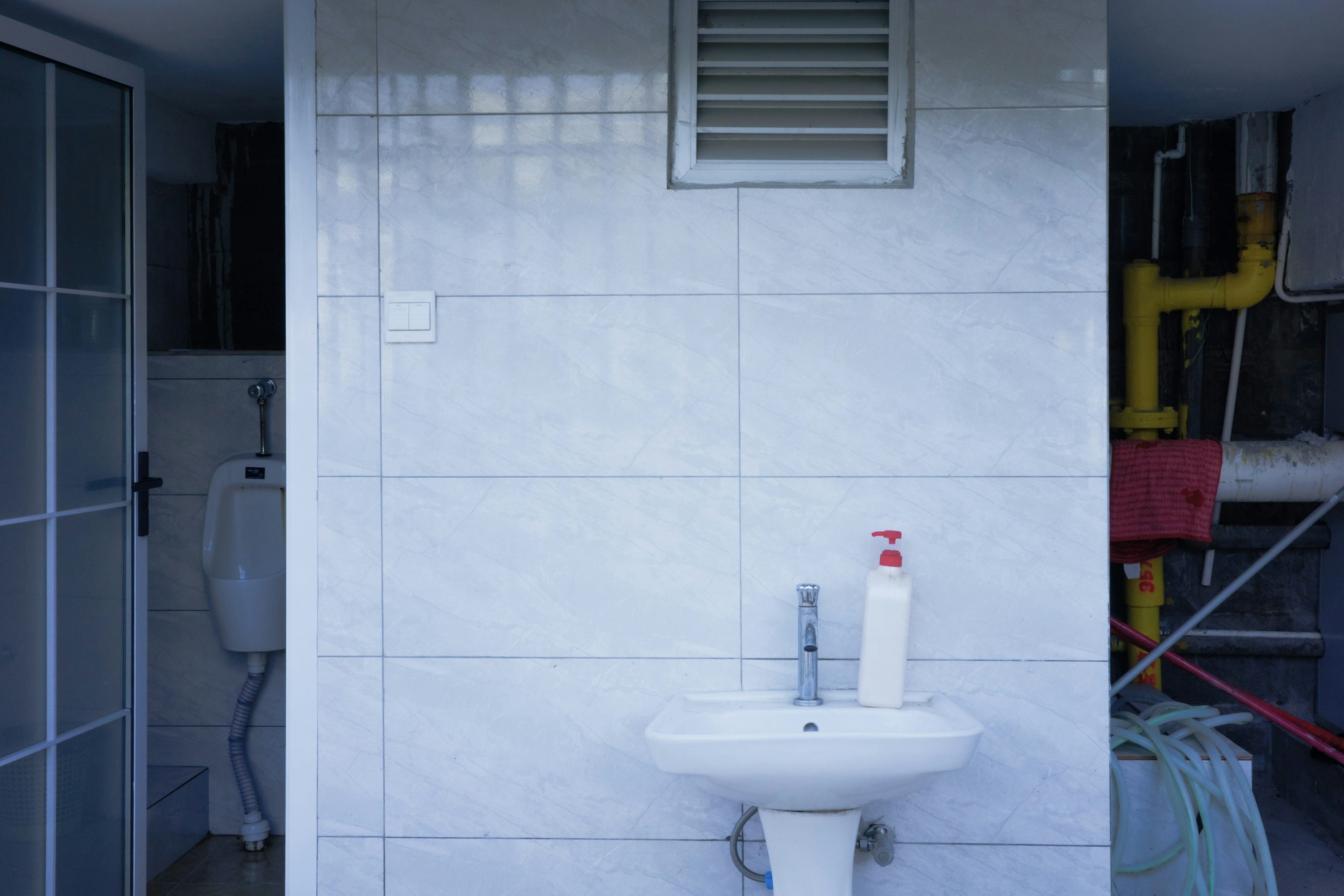 A white utility sink with exposed plumbing in a tiled room